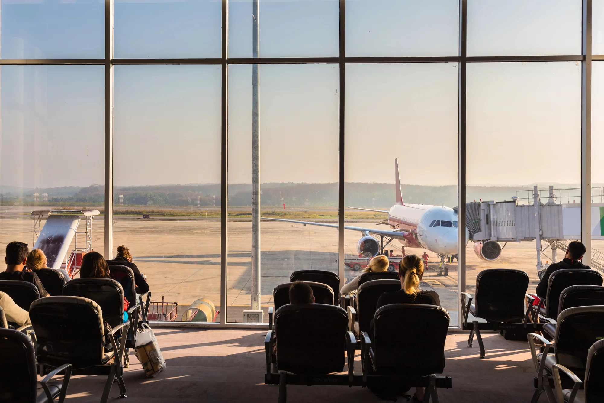 Des passagers attendent un avion derrière une vitre où l'on voit un avion sur le tarmac.